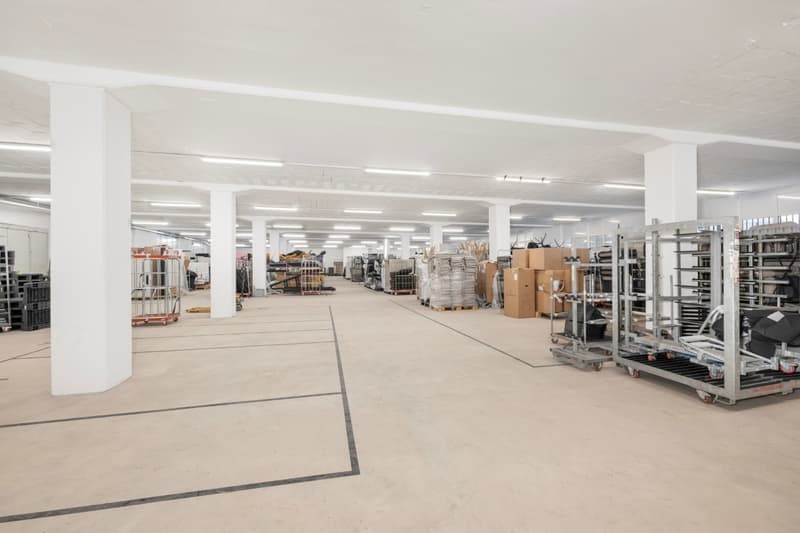 large open space, white pillars, white ceiling, fluorescent lighting, storage boxes, trolleys, shelves
