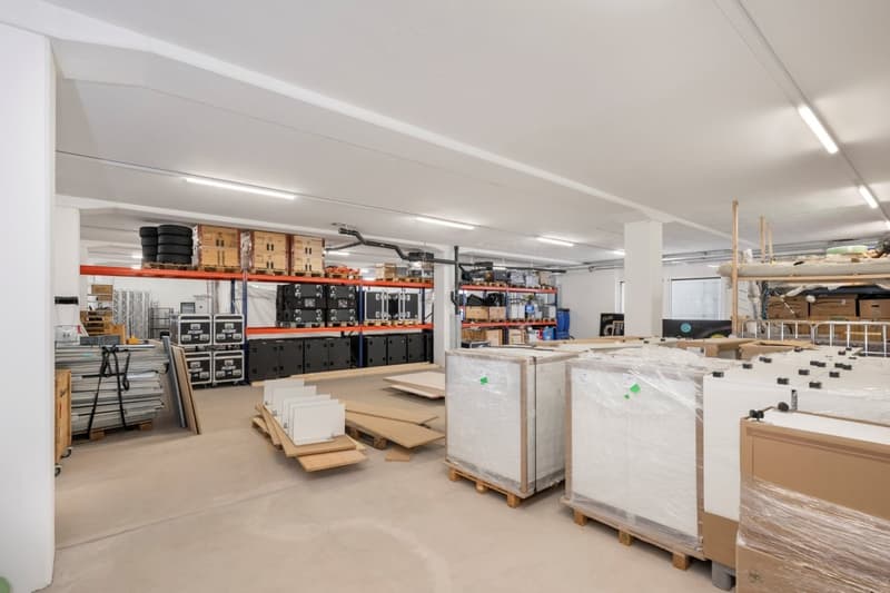 Warehouse with white walls, high ceiling, multiple shelves, storage boxes, and wrapped items