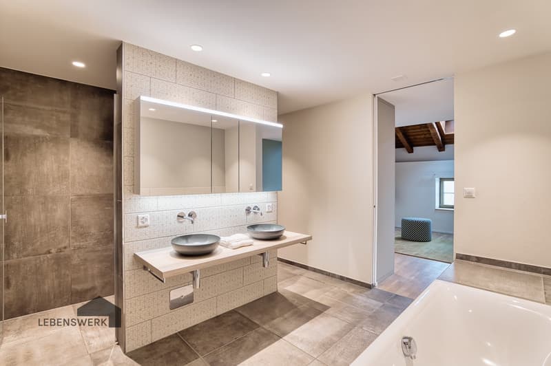 Das grosszügige Masterbad en Suite überzeugt mit Badewanne, begehbarer Dusche mit Glaswand, einem eleganten Doppellavabo und hochwertigen Armaturen