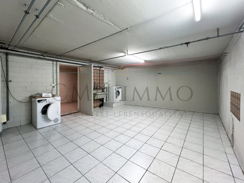 two washing machines, tiled floor, ceiling pipes, white walls, sink