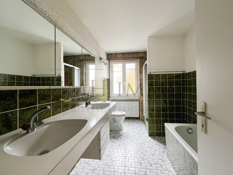 modern bathroom with white tiles, green tiles, white sink, white bathtub, white toilet, large mirror