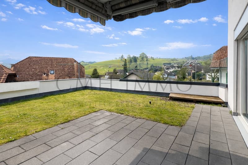 Tiled terrace with grass, partial wall, bench, clear view of surrounding area