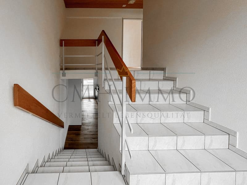White tiled staircase with wooden handrail, white walls, wooden floor at the bottom
