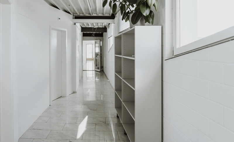 white walls, white tiled floor, a shelf with a plant on top, a window, a potted plant on the right