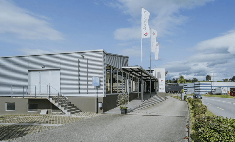 An industrial looking building with corrugated metal siding, large front window, double doors, stairs on either side, and a canopy to the entrance