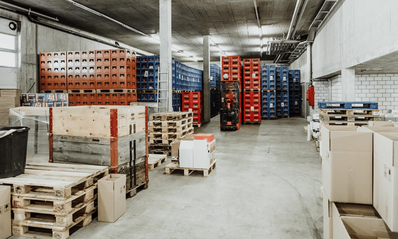 A large warehouse space filled with pallets, crates, and storage boxes, a forklift is present