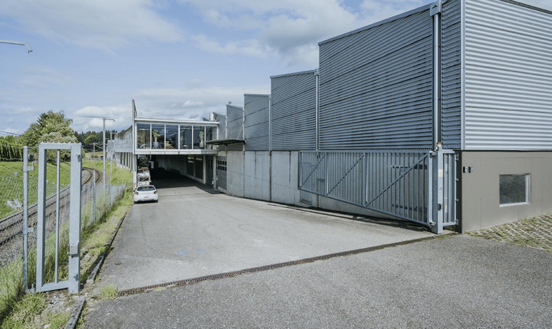 Warehouse with glass windows, metal siding, and entrance gate, with a car leaving through the entrance