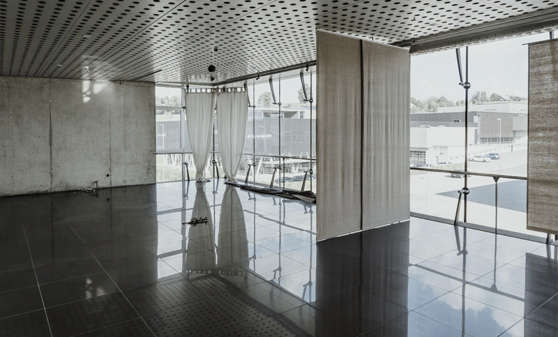 Wide open space with gray tile flooring, large windows, and curtained sections. Large reflection on the tile floor.