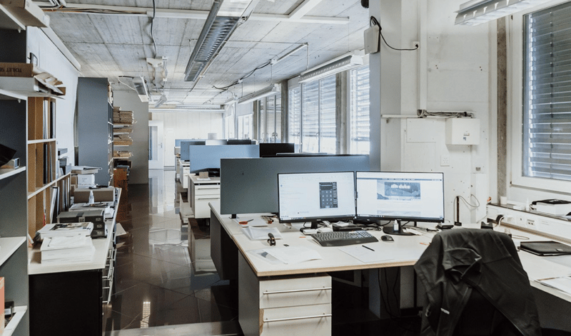 Spacious office with multiple cubicles, white walls, gray ceiling, and black tile floor, modern furniture and equipment.