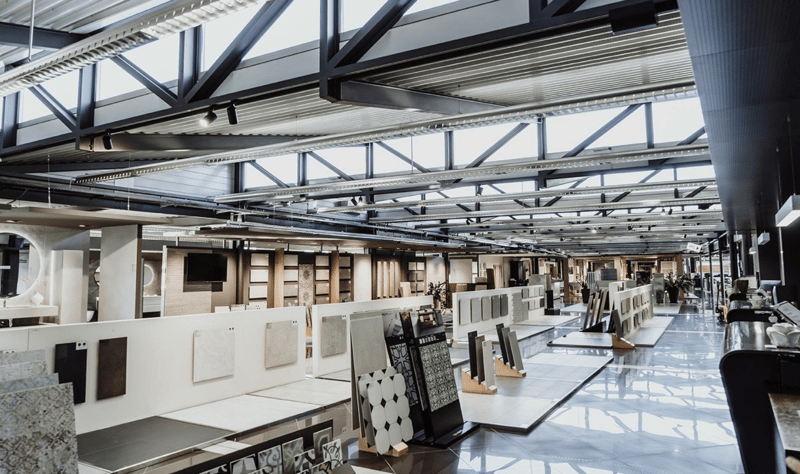 Modern, spacious interior with high ceilings, exposed metal beams, large windows, white walls, grey flooring, display stands, and lighting fixtures