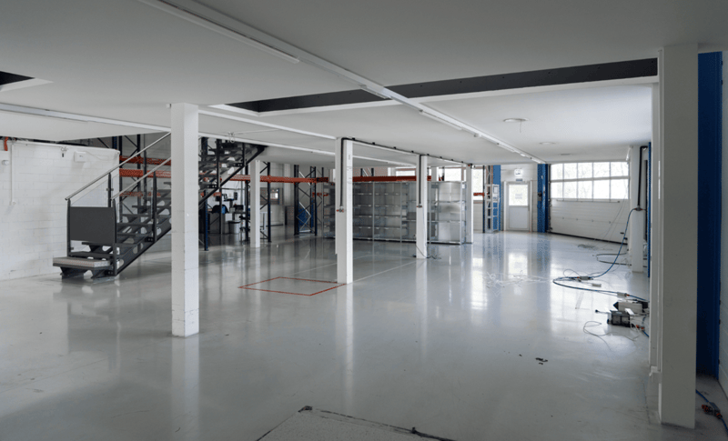 Spacious warehouse with bright lighting, white walls, large steel shelves, and a staircase.