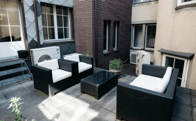 two black couch with white cushion, one glass table, potted plants, tiled flooring, stairs, two air conditioners