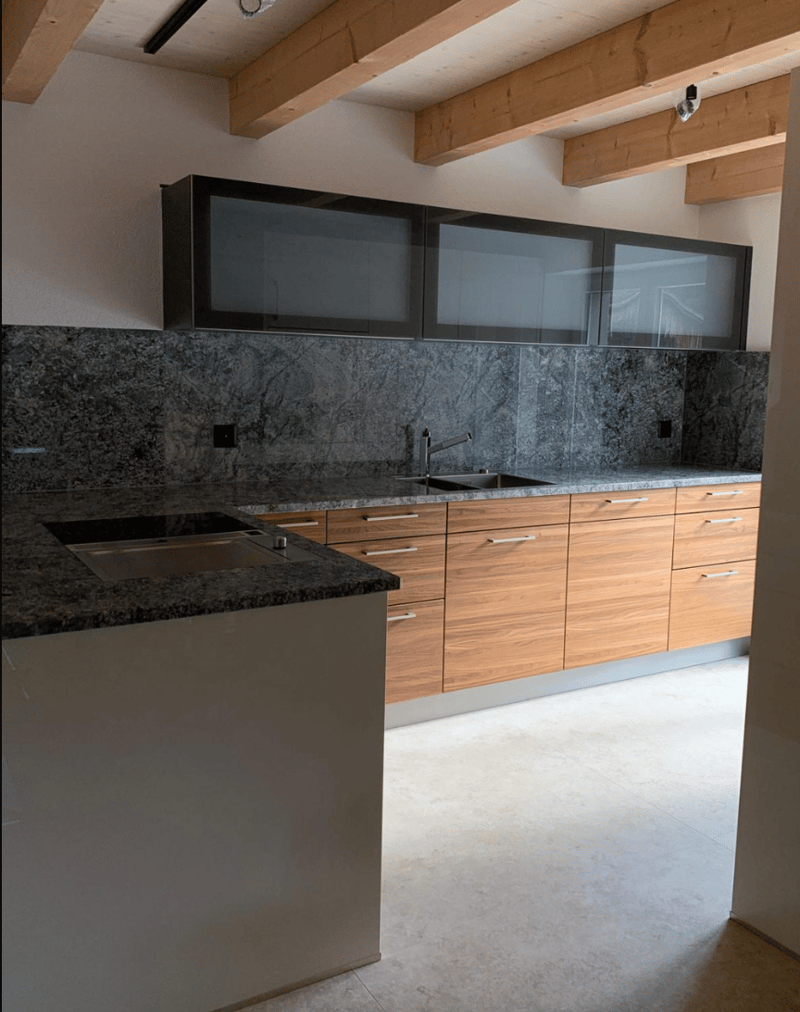 Modern kitchen with gray granite countertops, wooden cabinets, glass doors, stainless steel sink, two sinks, exposed wooden beams.