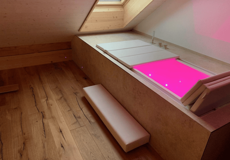 A small, cozy room with an illuminated bathtub and wooden floors