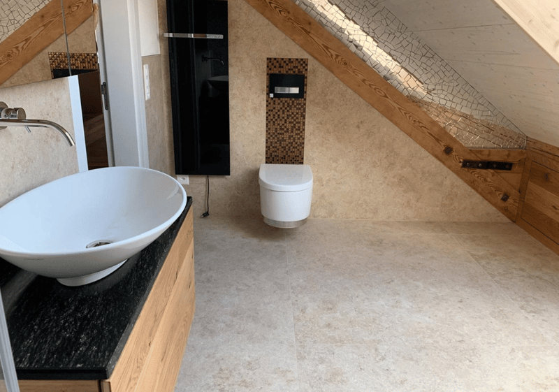 a bathroom with a sink, toilet, wooden ceiling and floor, beige tiles, a black countertop