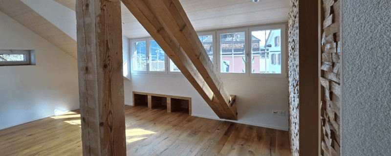 Wooden floor, two large windows, wooden beam, bench, wooden wall paneling