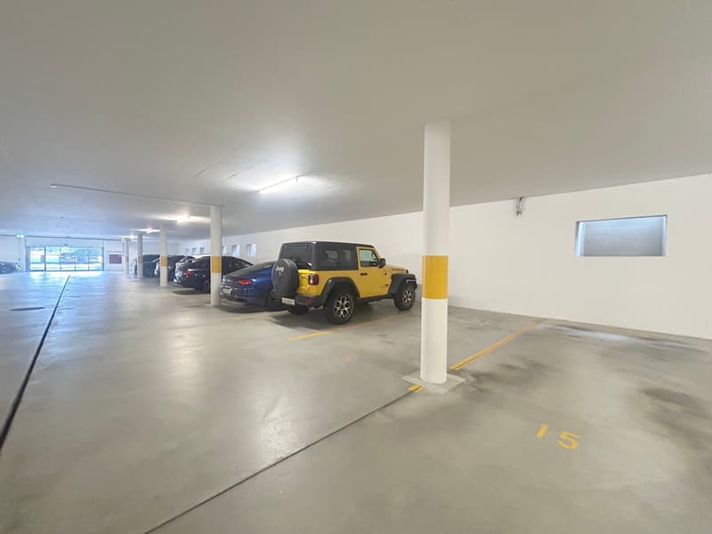 underground parking lot with several cars parked, white walls, yellow markings, pillars