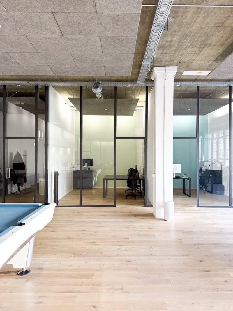 Spacious open plan office with glass walls, hardwood flooring, large desk, and a pool table in the corner.