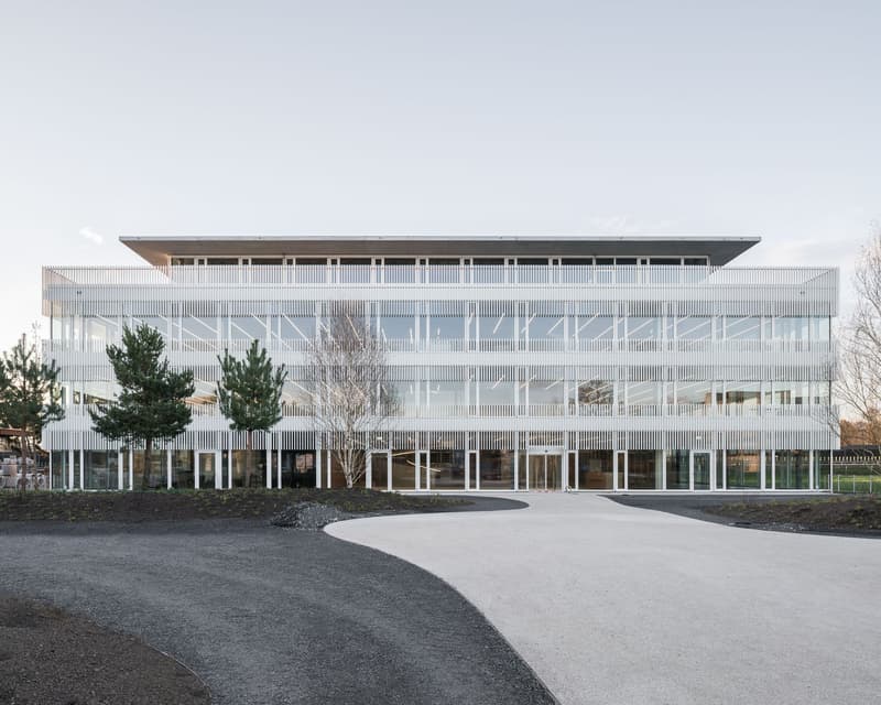 Modern office building, large glass windows, multiple floors, curved driveway, several entrance points, symmetrical design, greenery around