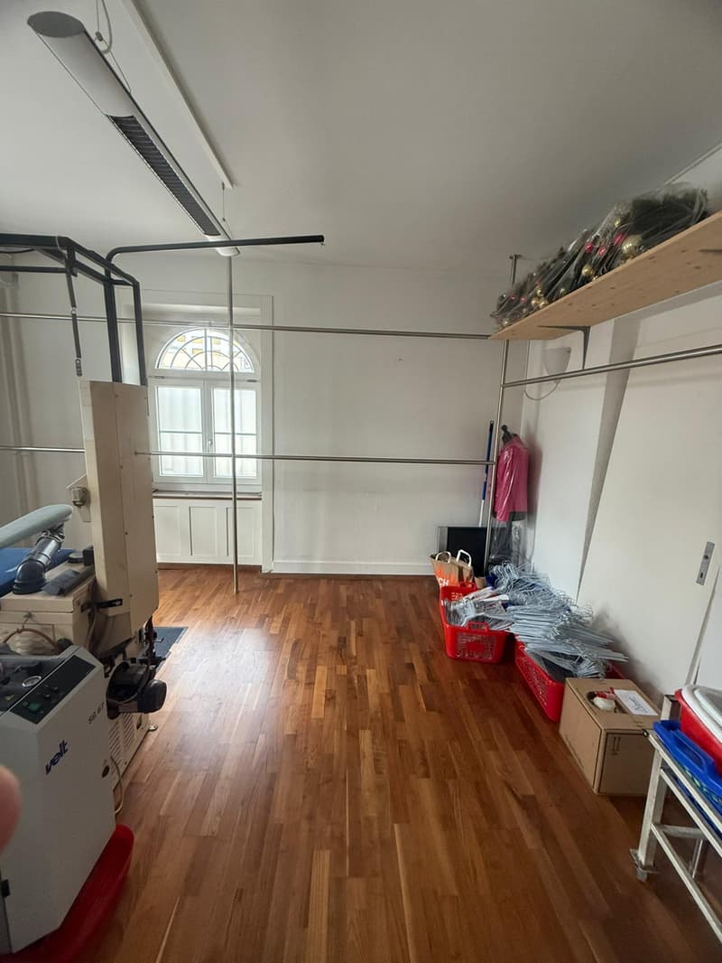Empty room with wooden floor, metal beams, shelves, storage boxes, and various items like a white air conditioning unit, white cabinet, and some plastic bags.