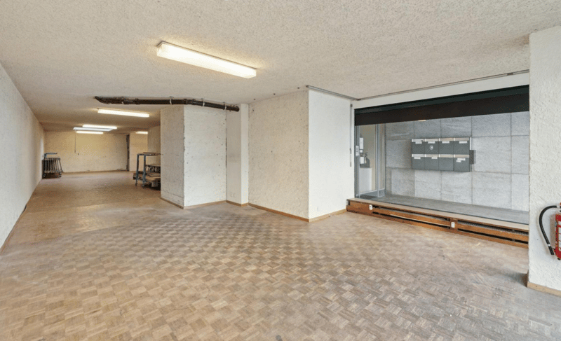 spacious corridor with concrete flooring, white walls, ceiling lights, mail slots, and a fire extinguisher