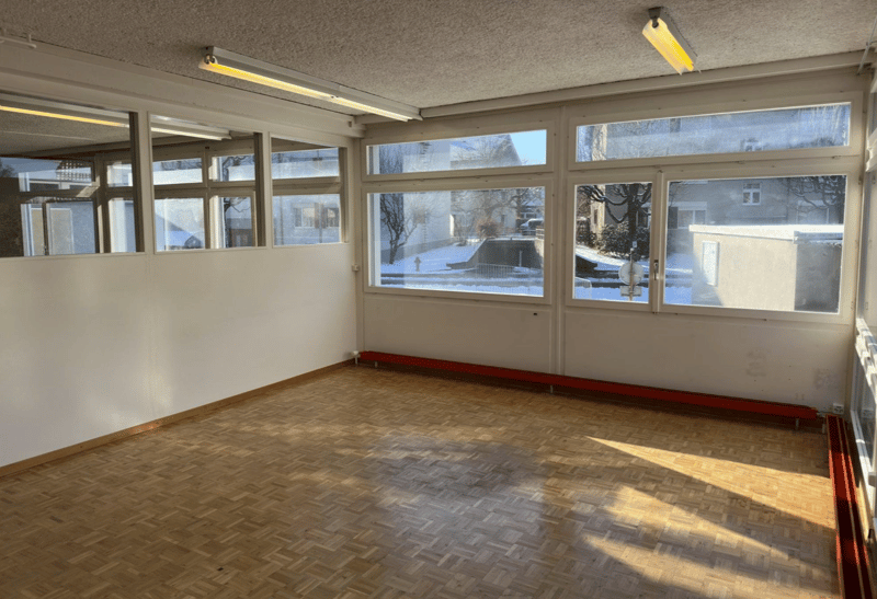 Empty room with parquet flooring, large windows, and fluorescent ceiling lights