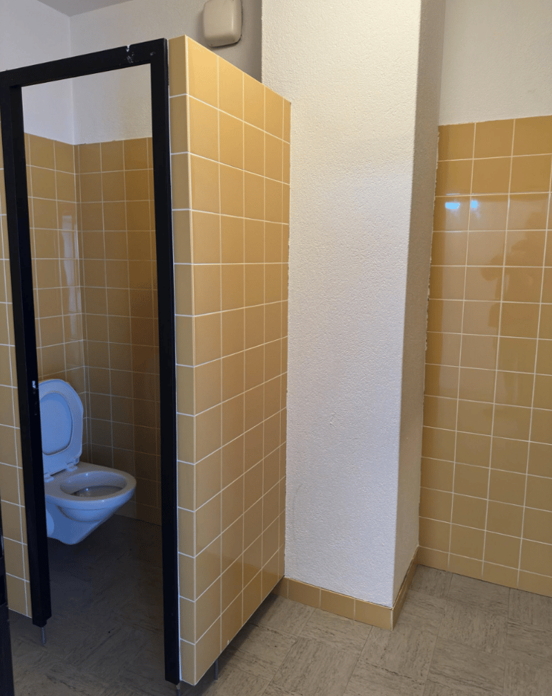 A small enclosed bathroom stall with tiled walls and a white toilet
