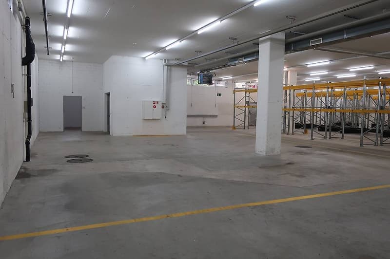 Empty warehouse with concrete floor, metal scaffolding, electrical panels, and white walls