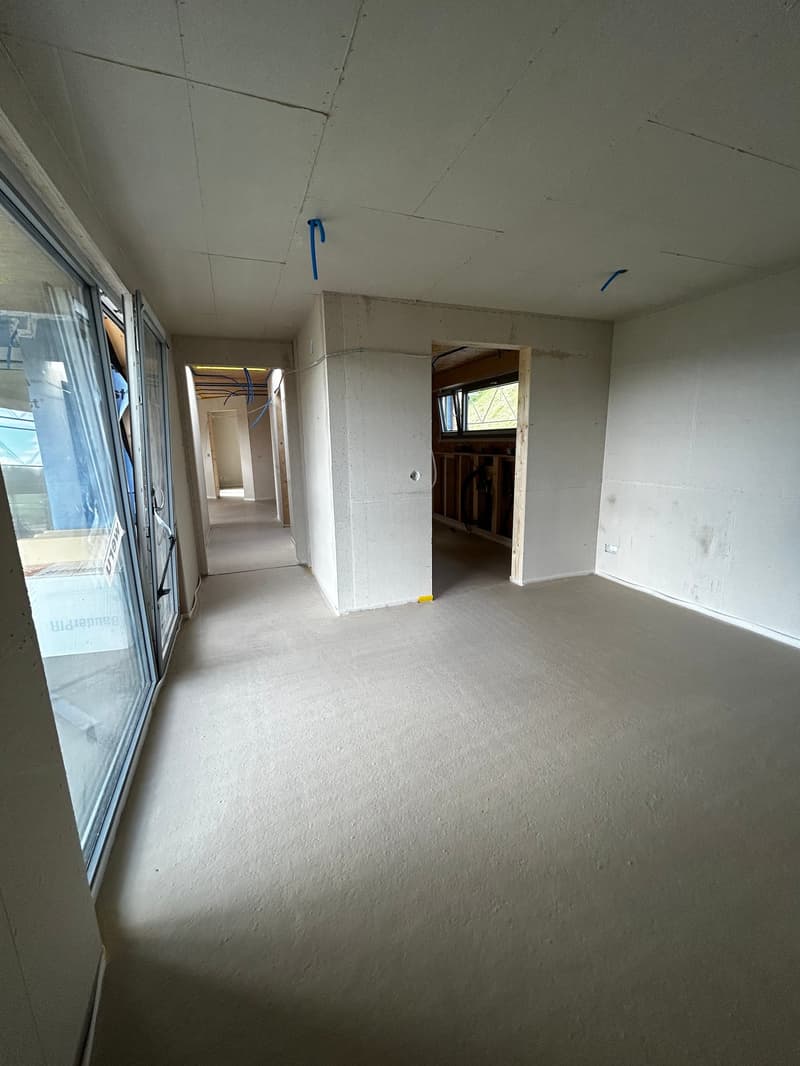 Empty room with white walls, ceiling, and floor, glass doors, and windows, and a hallway leading to other rooms.