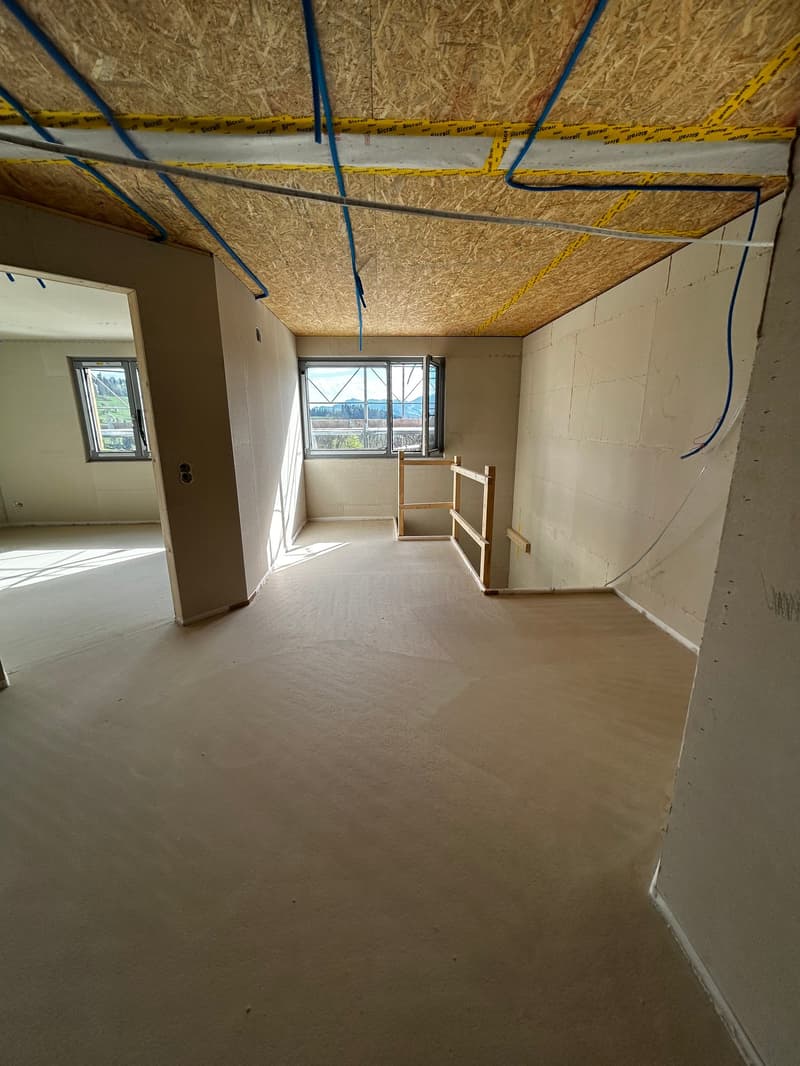 Empty room, unfinished, with exposed ceiling, walls, and floor, two windows, wooden handrail