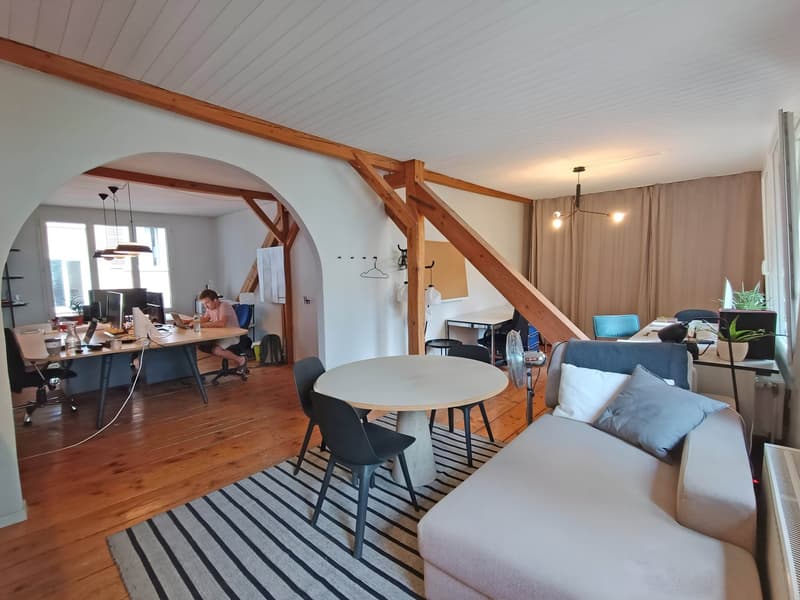 large open room with wooden floor, modern furniture, desks, couches, windows, plants