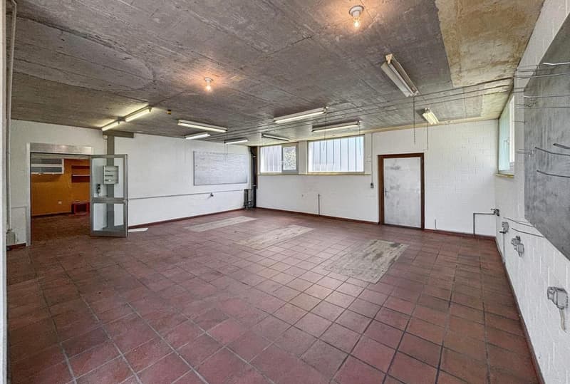 large empty room, red tiled floor, white walls, ceiling lights, two doorways, windows, whiteboard on wall