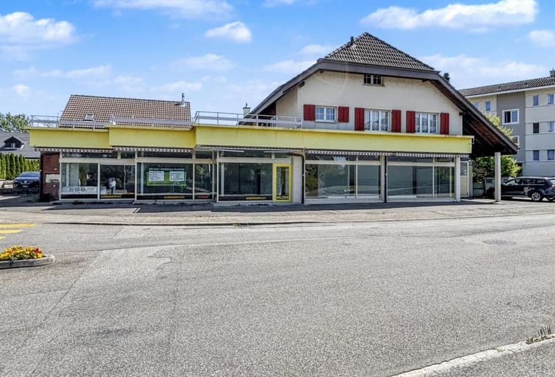 Two-story commercial building, glass windows, yellow awning, red shutters, rooftop terrace, parking area