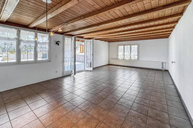 large room, wooden ceiling, large windows, tiled floor, sliding glass doors leading to a balcony