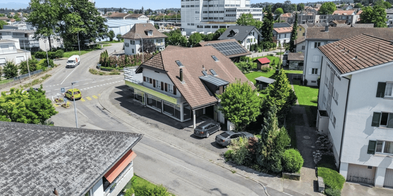 Aerial view of houses, trees, gardens, solar panels, street, parked cars, and building with swimming pool