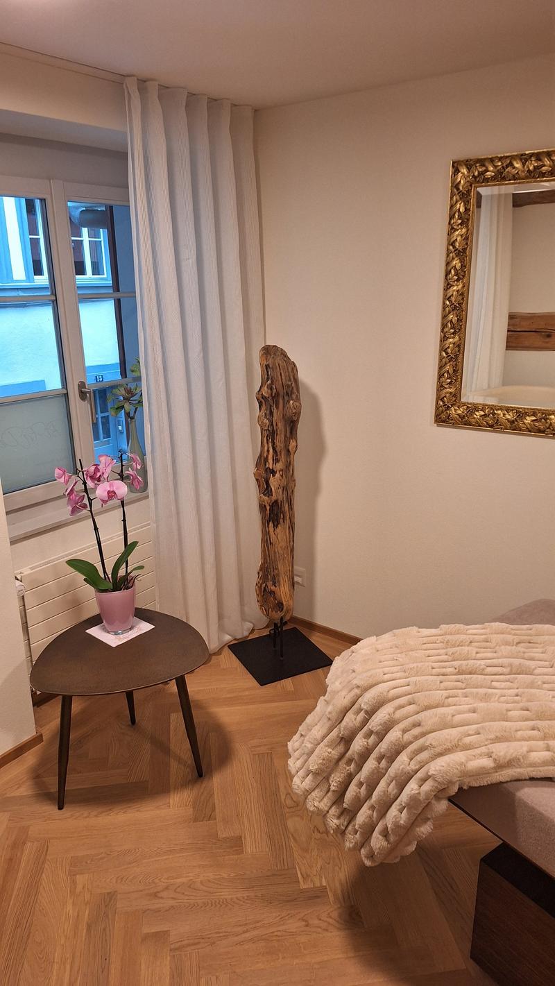wooden floor, side table, white walls, window, radiator, mirror, table with flower