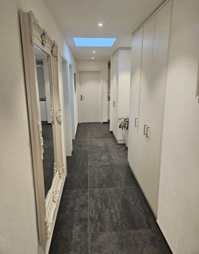 empty corridor, tile flooring, large mirror, white wall, small light above corridor, closed door