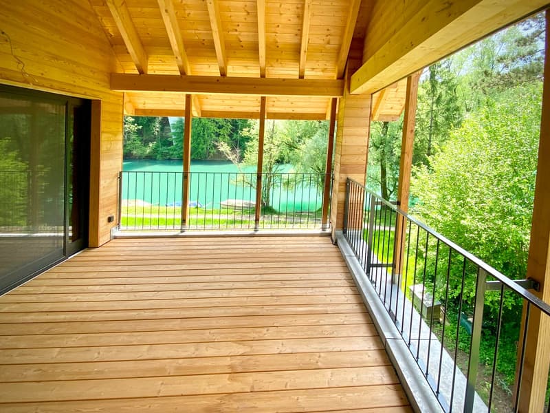 Large wooden balcony with railings, wooden floor, glass doors, view of the lake