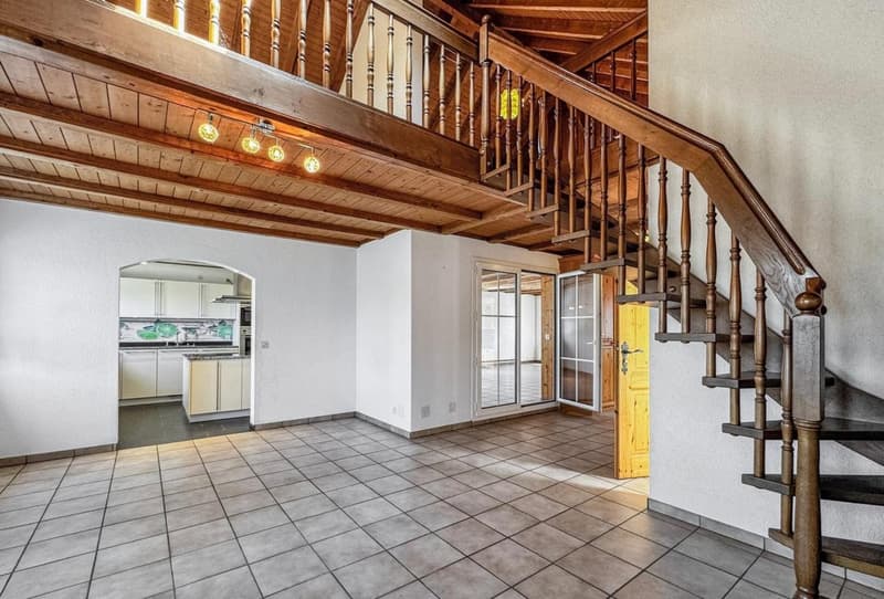 Empty room with wooden staircase, tiled floor, white walls, kitchen area with cabinets and countertop