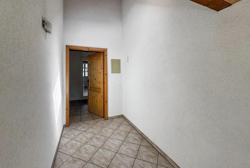 Empty hallway with tiled floor, wooden door, white walls, light coming from the hallway