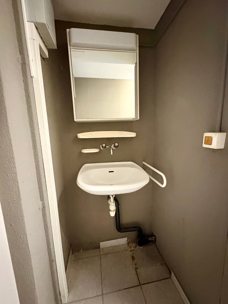 A small room with a white sink, mirror, and a shelf attached to the wall
