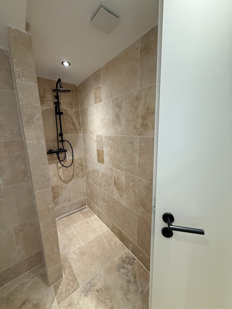 shower room with beige tiles, black shower head, drain in the floor