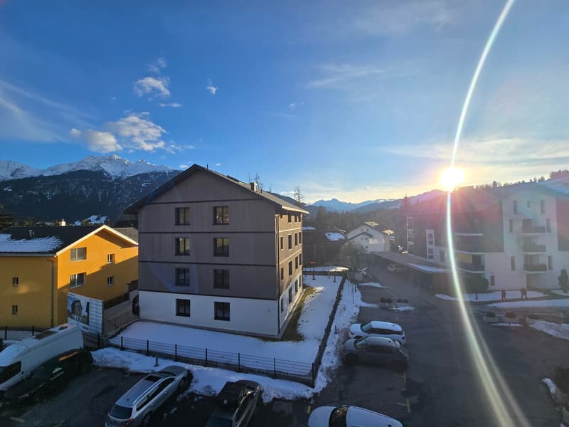 A three-story building with a parking lot in front, surrounded by snow-covered mountains