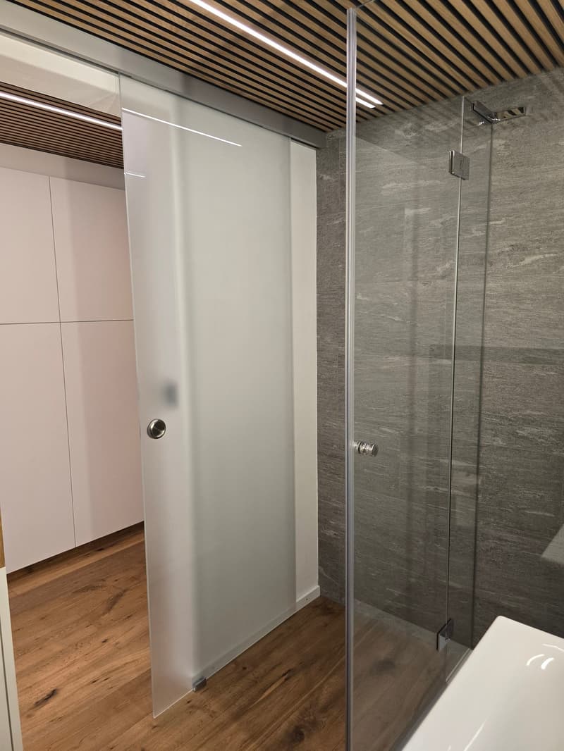 shower room with glass door, wooden floor, white wall, white sink