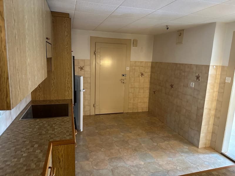 empty kitchen with wooden cabinets, tiled floor, tiled wall, sink, refrigerator, door