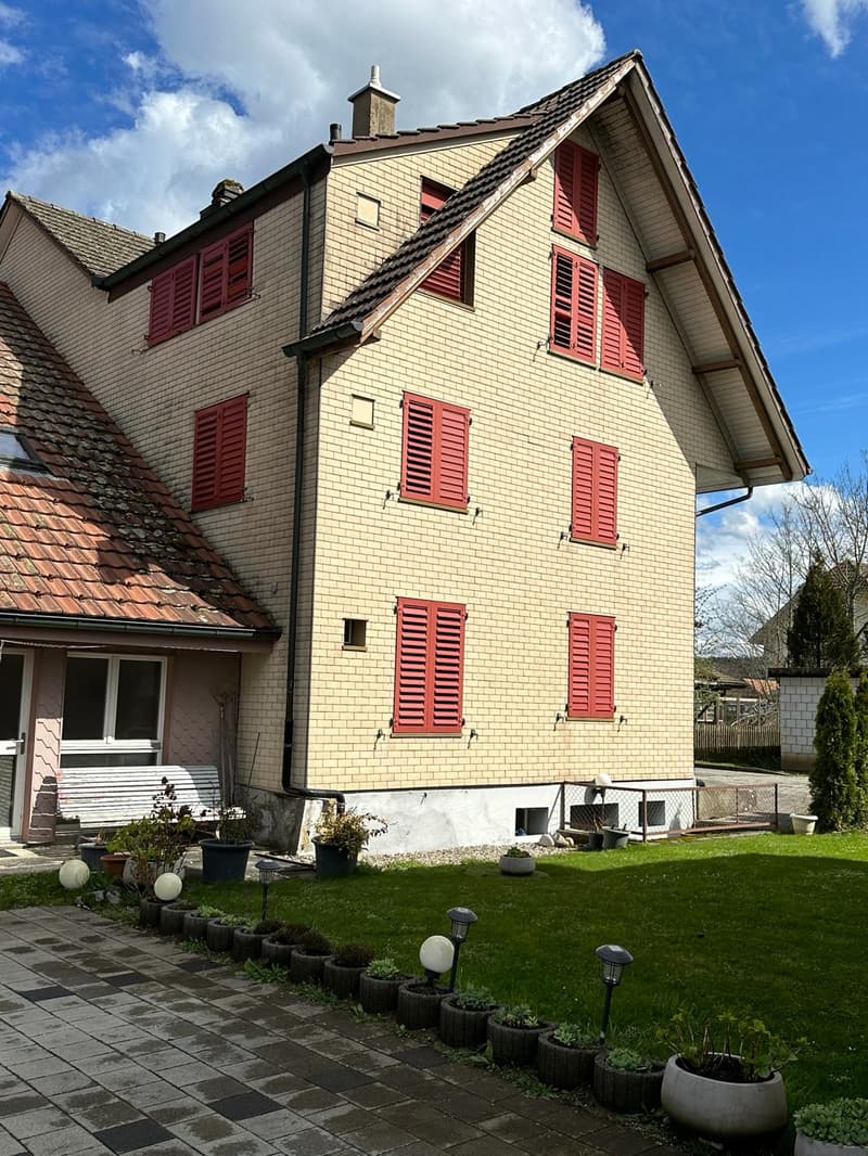 2 story house, red shutters, brick wall, red roof, garden with plants and lawn