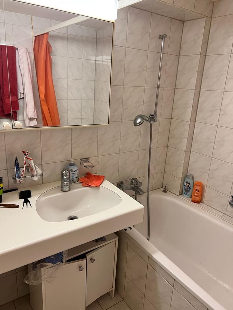 Bathroom with white tiles, white sink, bathtub, mirror, and shower head.