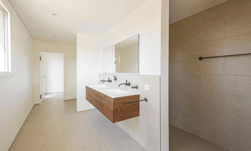 Bathroom with white walls, wooden cabinet, double sink, mirror, and shower area