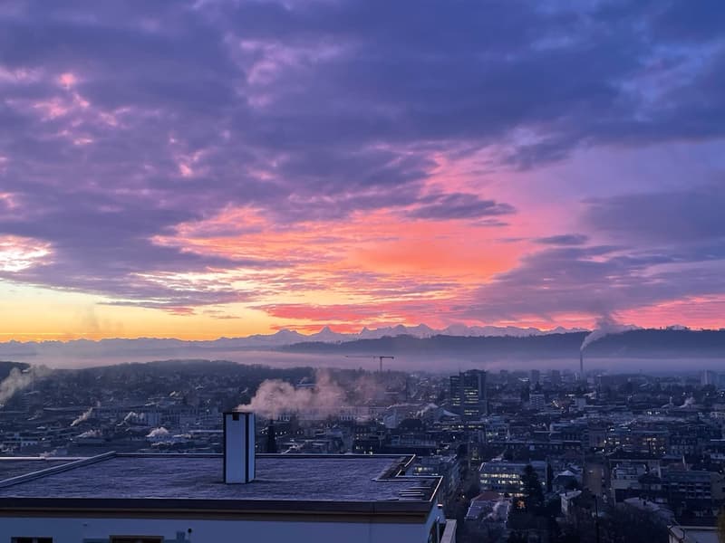 Aerial view of a city with a sunset, mountains in the distance, and a cloudy sky.