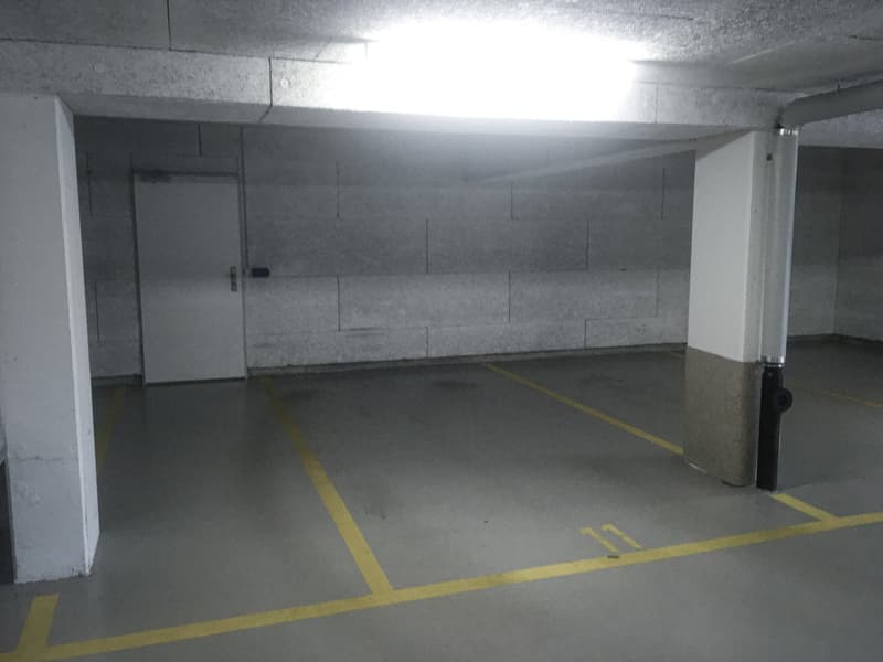 Empty parking space with yellow lines, white walls, and a white door.